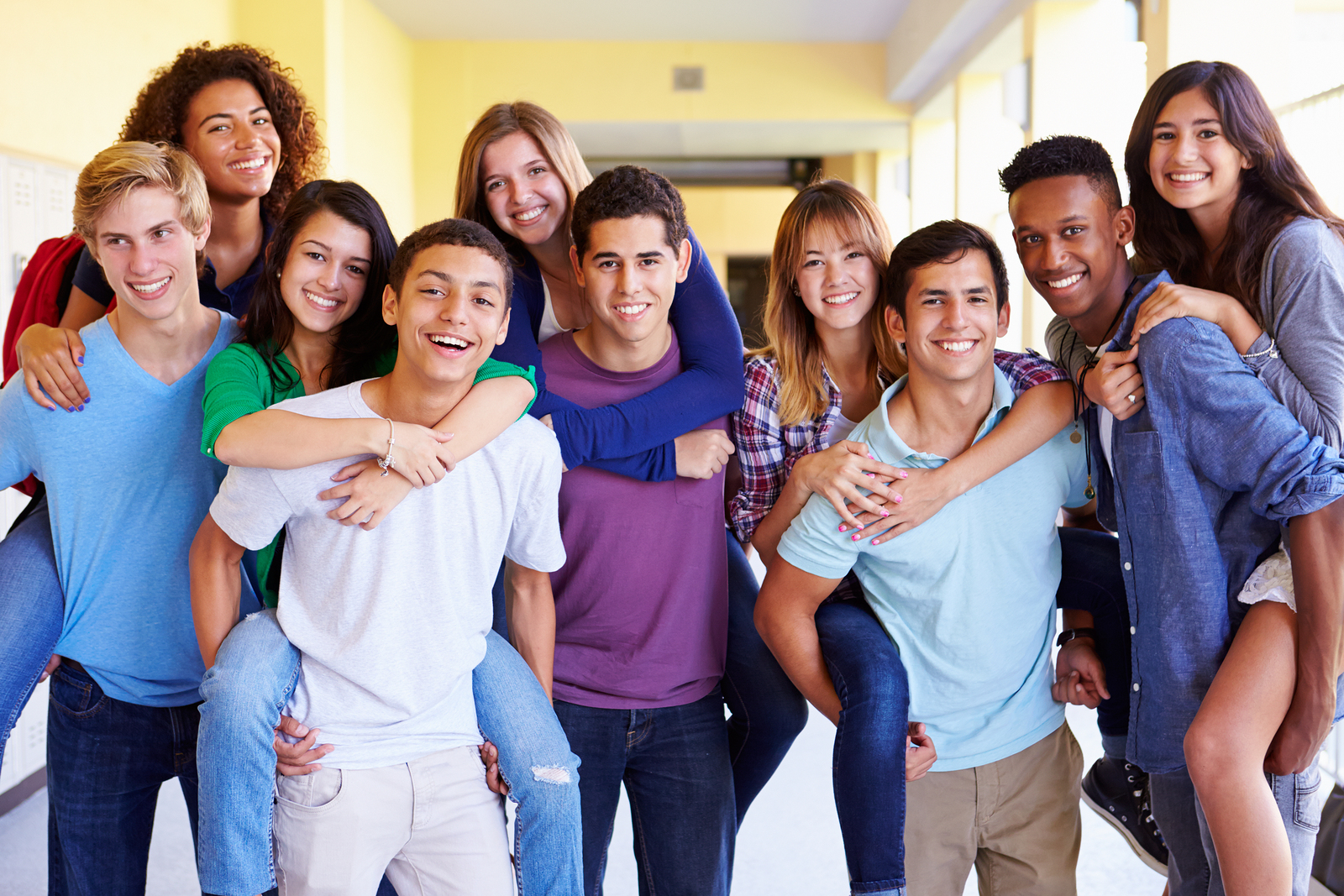 From Renew Hope and Healing: A group of smiling teenagers posing in a school hallway, with four girls giving piggyback rides to boys and others standing close together.