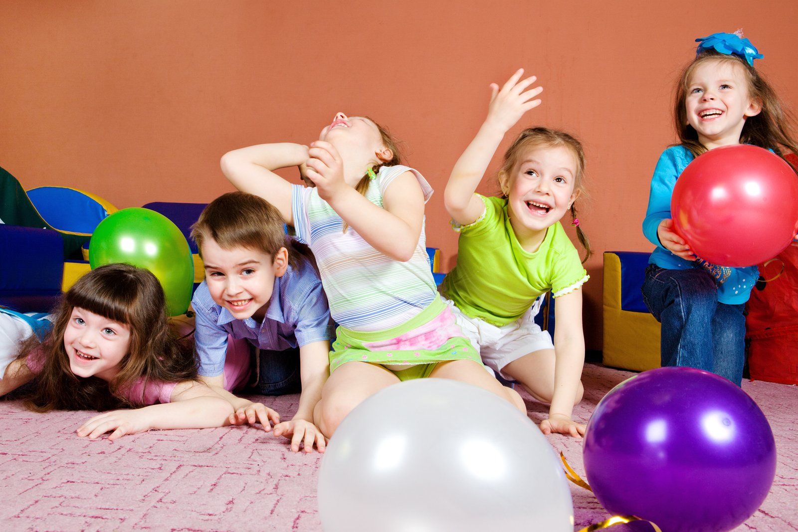 From Renew Hope and Healing: Five children play and laugh on a carpeted floor with colorful balloons scattered around them in a brightly lit room.