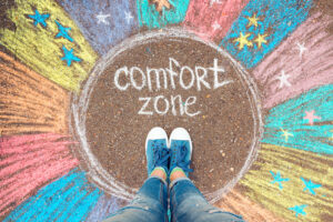 An individual standing hesitantly at the edge of a circle labeled 'Comfort Zone', looking ahead towards an expansive, bright horizon symbolizing new opportunities and growth.