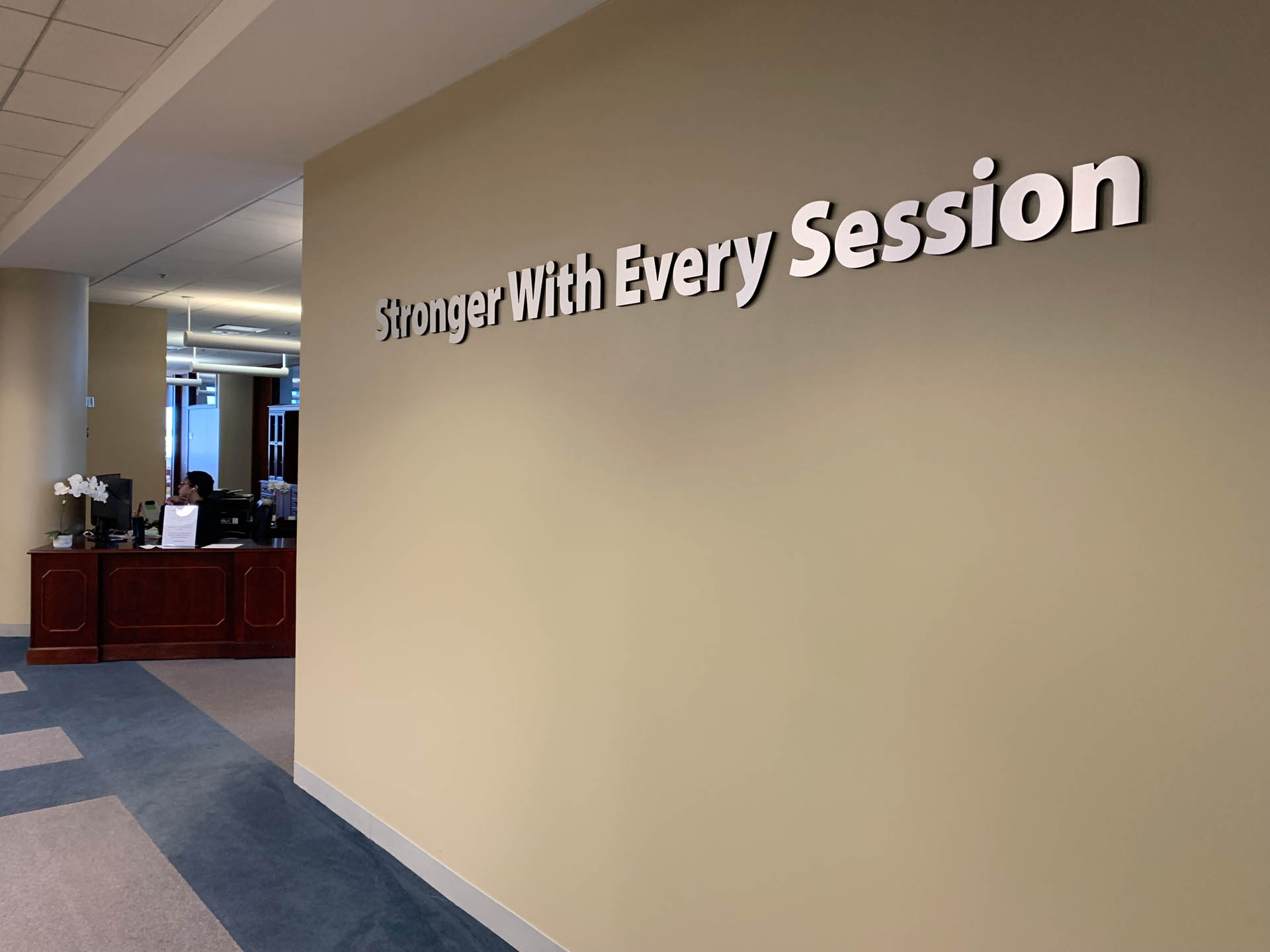 From Renew Hope and Healing: Office interior with a beige wall displaying the phrase "Stronger With Every Session" in large letters; a reception desk is visible in the background.