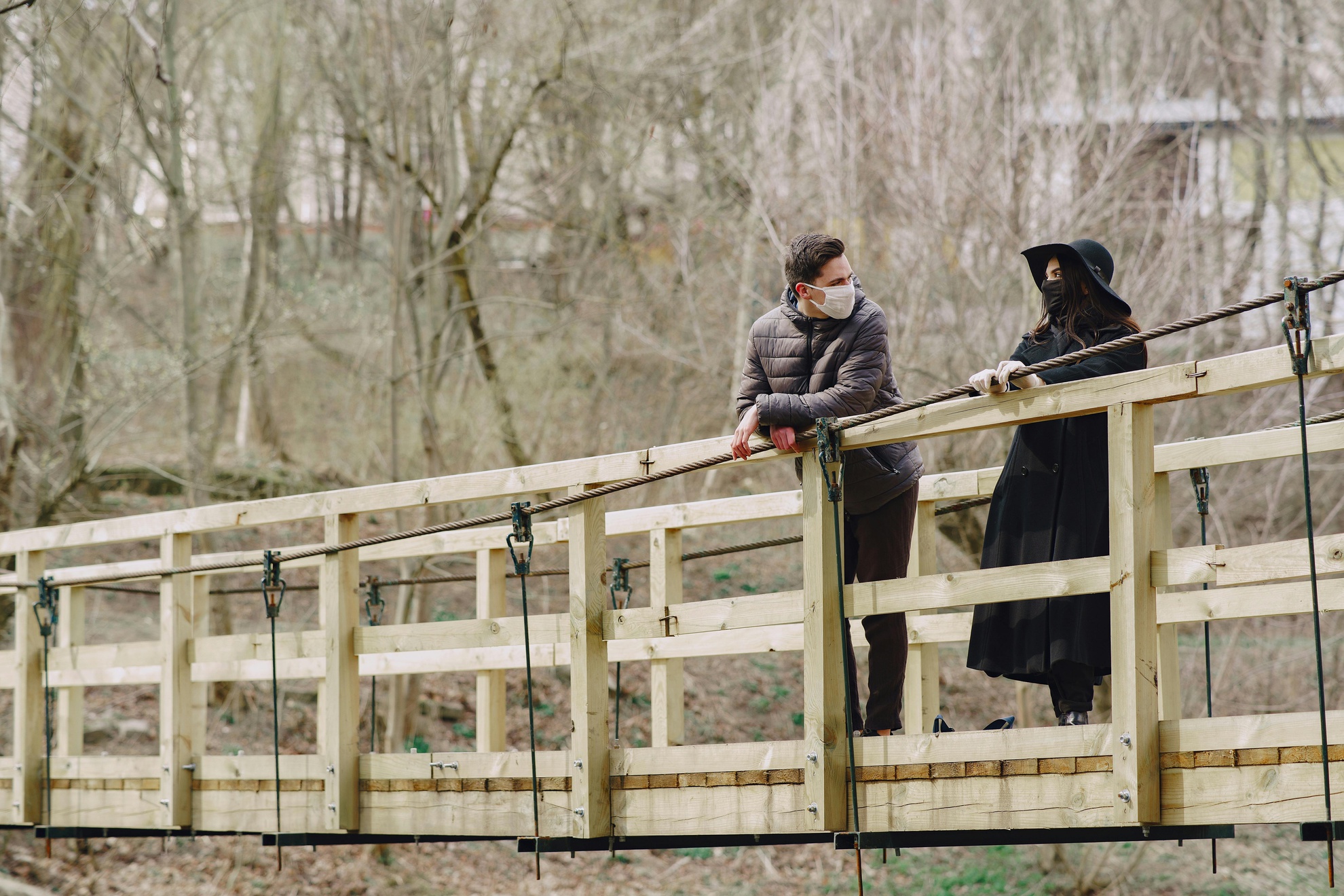 From Renew Hope and Healing: Two people participating in Adult Therapy stand on a wooden bridge in a forested area, facing each other and talking. The background features leafless trees and muted natural colors.