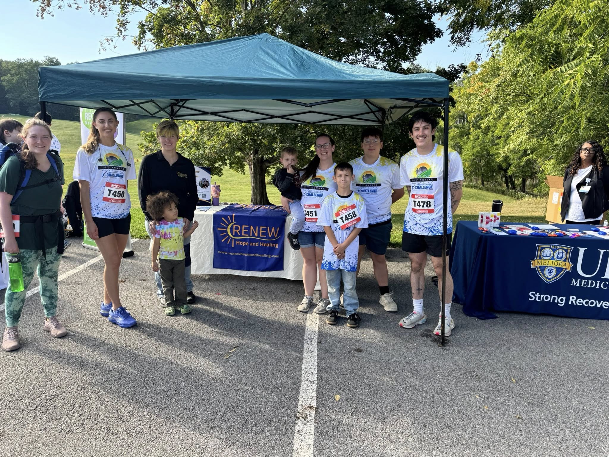 From Renew Hope and Healing: A group of people, some wearing race bibs and athletic clothing, stand in front of booths with "RENEW" and "UConn Health" banners at an outdoor event focused on promoting teen mental health.