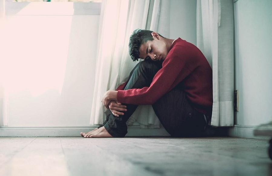 From Renew Hope and Healing: A person sits on the floor by a window, hugging their knees and resting their head on them, appearing deep in thought—reflecting the quiet introspection often encouraged in adult therapy.