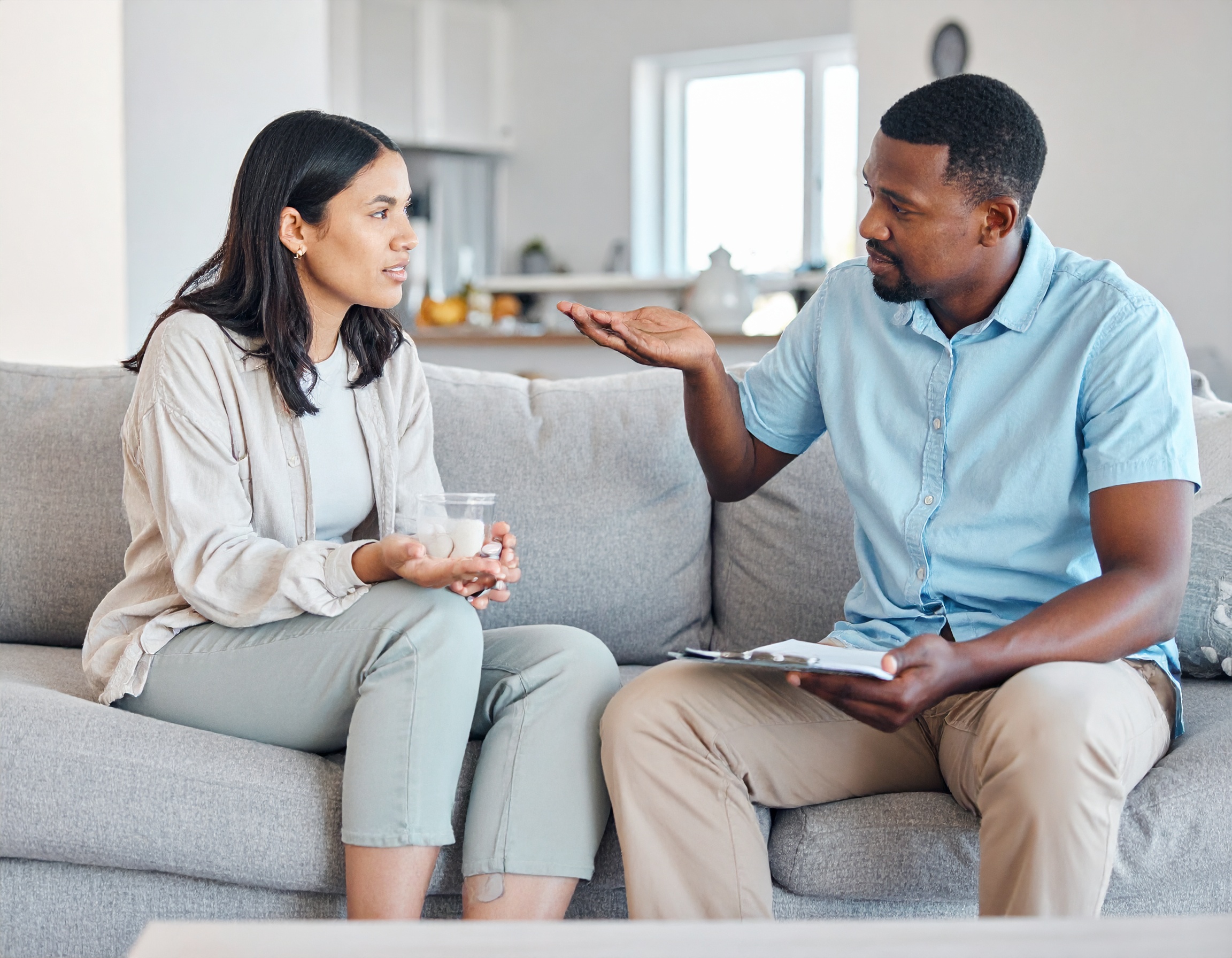 From Renew Hope and Healing: Two people sit on a couch having a serious conversation; one holds a glass of water while the other, likely guiding a couples counseling session, gestures thoughtfully with a clipboard.