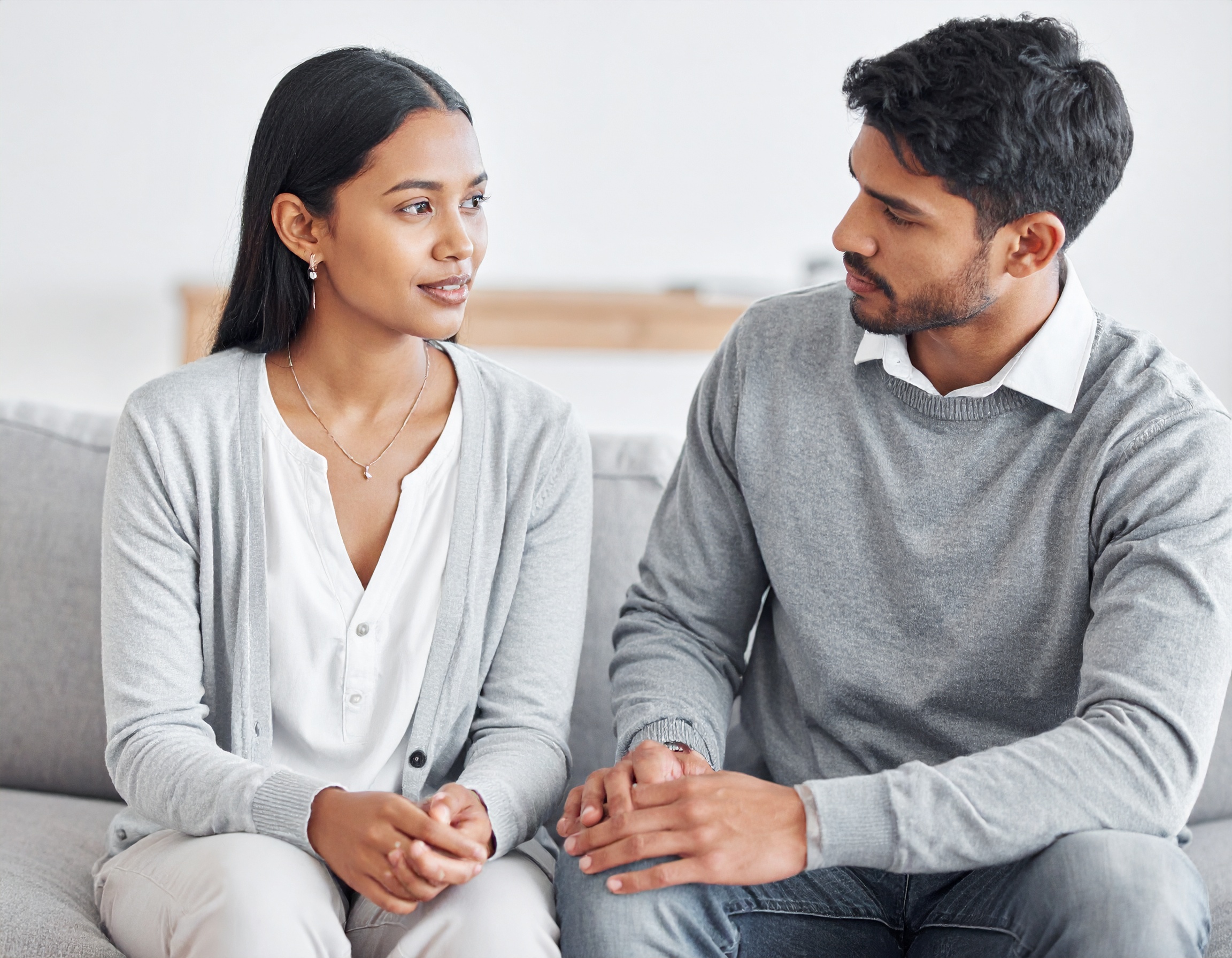 From Renew Hope and Healing: A woman and man sit on a sofa facing each other, engaged in a serious conversation while holding hands, reflecting the intimacy often seen in Couples Counseling.