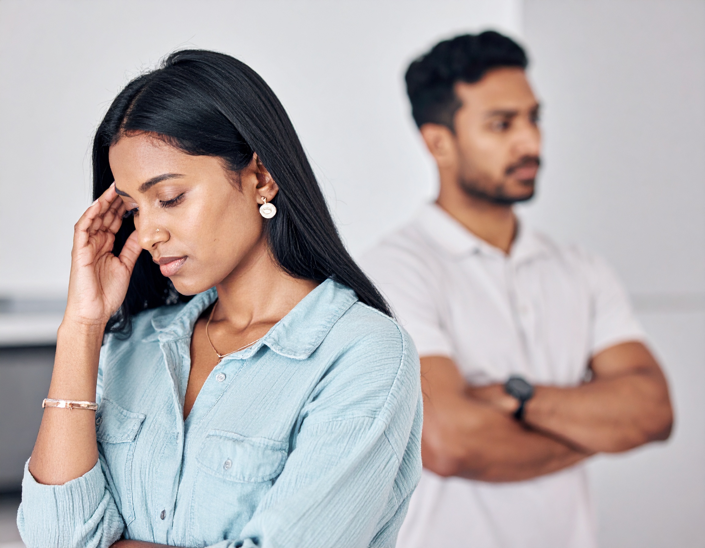 From Renew Hope and Healing: A woman stands in the foreground looking down with her hand on her head, while a man stands behind her with his arms crossed, both appearing upset—highlighting the need for couples counseling or relationship therapy.