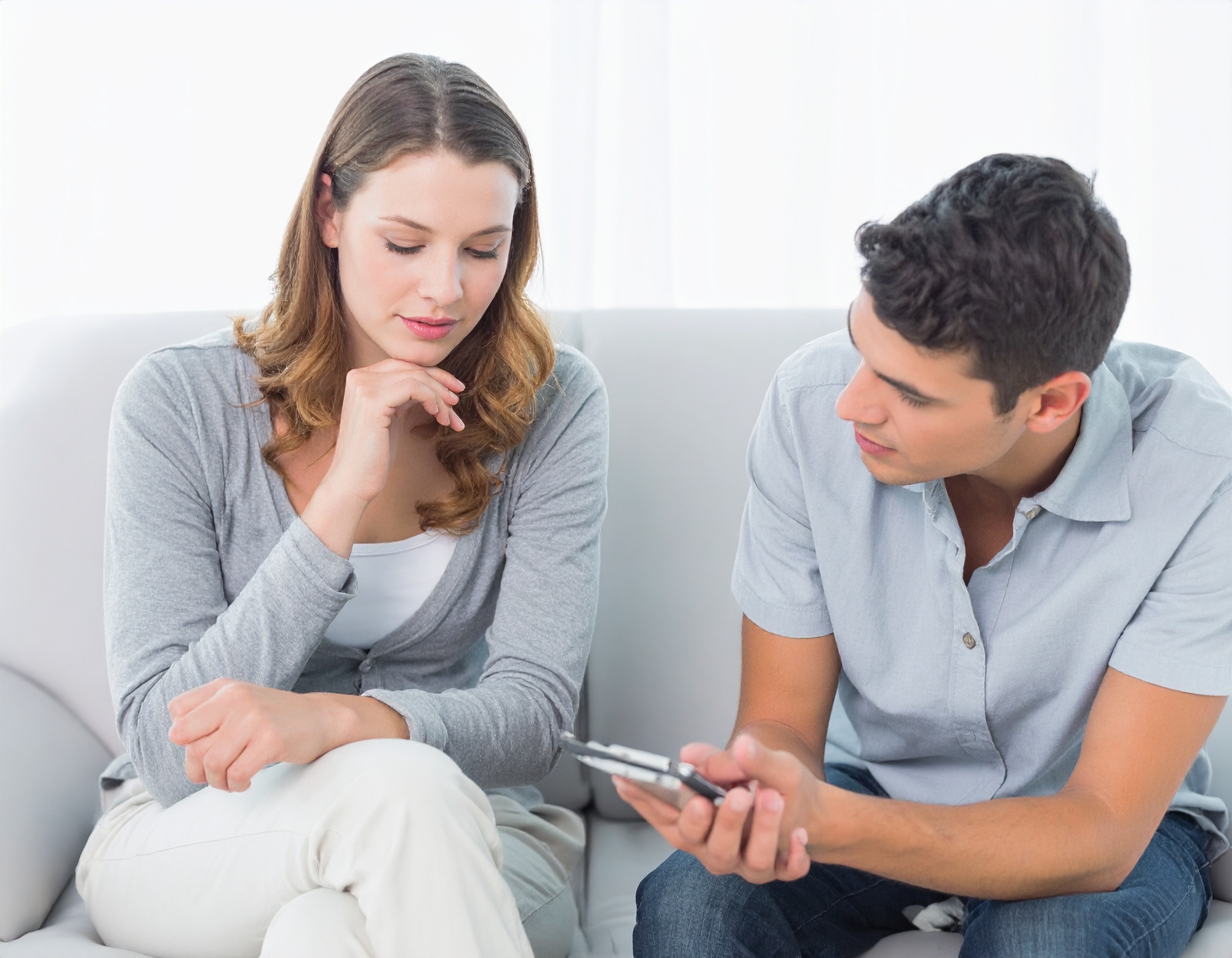 From Renew Hope and Healing: A man and a woman sit on a couch. The man is showing something on his phone to the woman, who listens attentively, reflecting a calm moment often seen in couples counseling sessions.