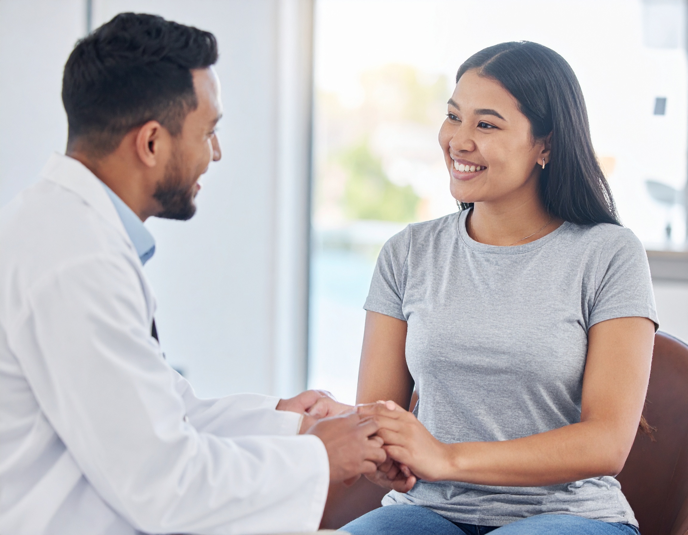 From Renew Hope and Healing: A doctor in a white coat holds hands with a smiling woman in a grey shirt during an Adult Therapy consultation in a bright office.