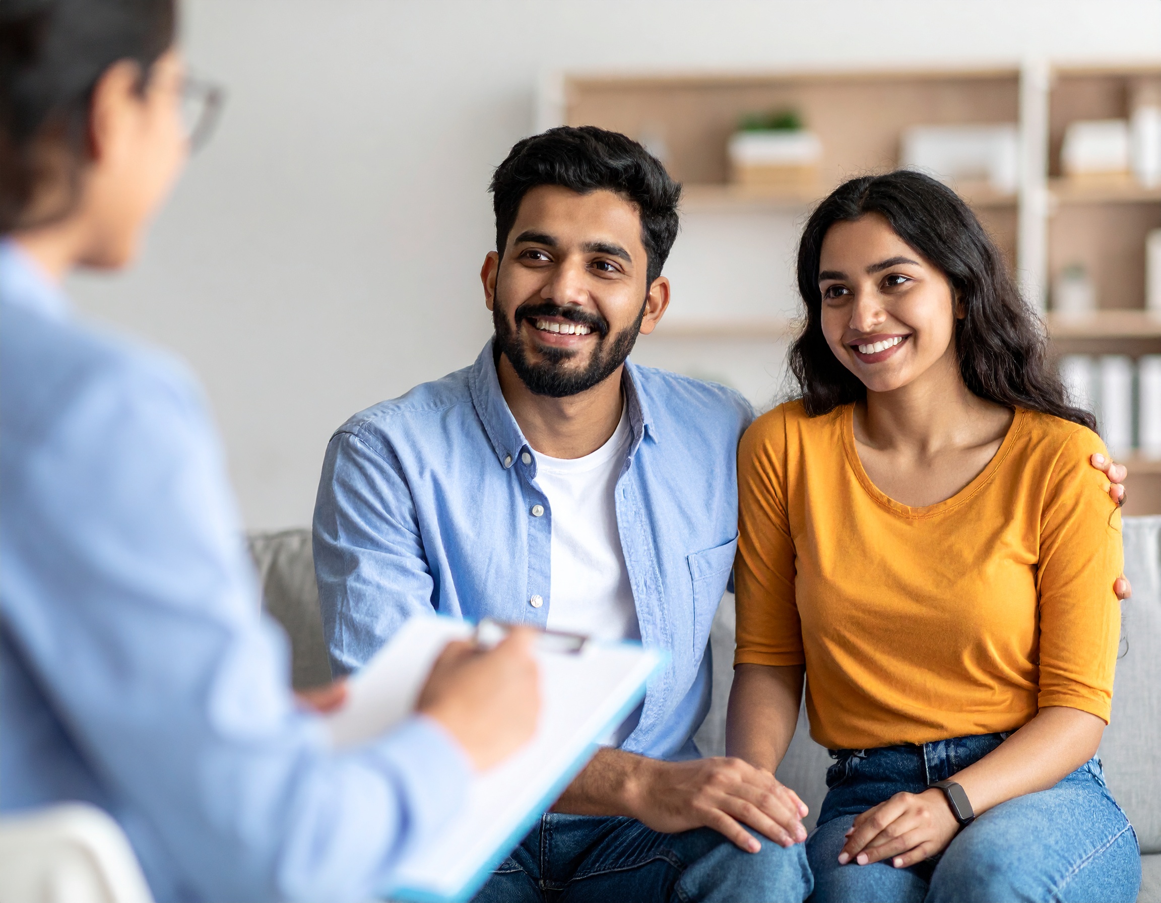 From Renew Hope and Healing: A couple sits together on a couch, smiling and talking to a professional holding a clipboard, suggesting a couples counseling or consultation session.