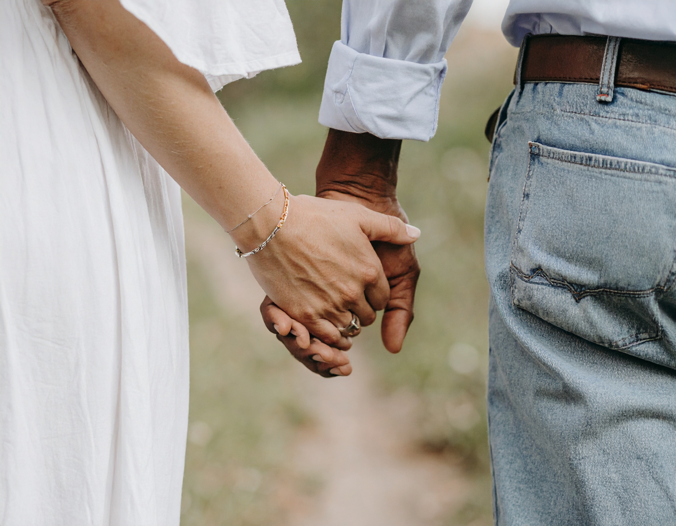 From Renew Hope and Healing: Close-up of two people holding hands outdoors, one in a white dress and the other in blue jeans and a light shirt—a warm moment that reflects the support found in couples counseling.