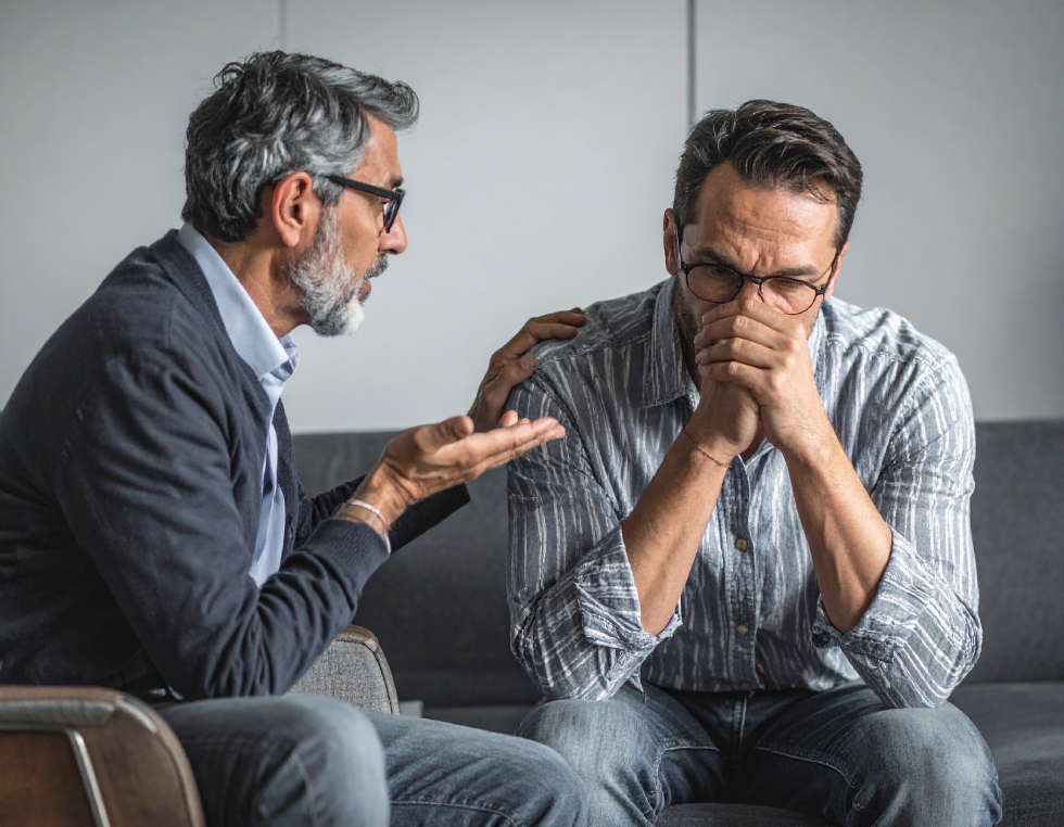 From Renew Hope and Healing: Two men sitting on a couch; one man is comforting the other, who appears distressed and has his hands over his mouth, reflecting a moment that could take place during depression counseling.