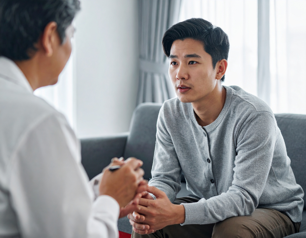 From Renew Hope and Healing: A man sits on a couch attentively listening to a counselor during an anxiety therapy session in a well-lit room.