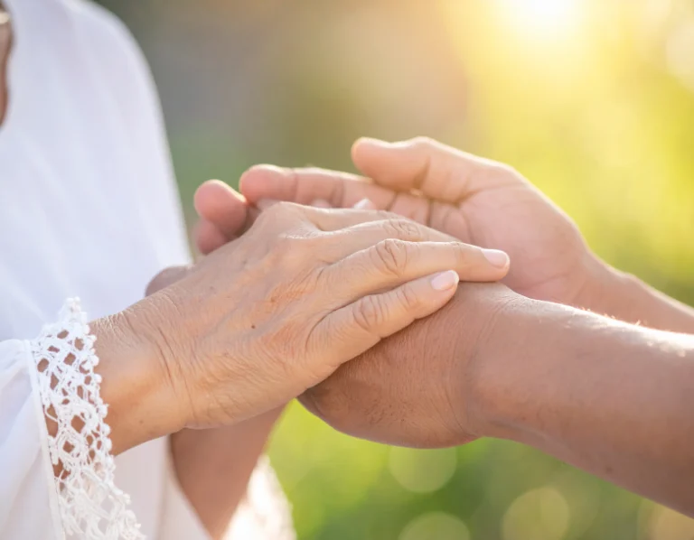From Renew Hope and Healing: Two people holding hands outdoors, one older with light skin and the other younger with darker skin, in soft sunlight—a moment that reflects the support and connection fostered through couples counseling.