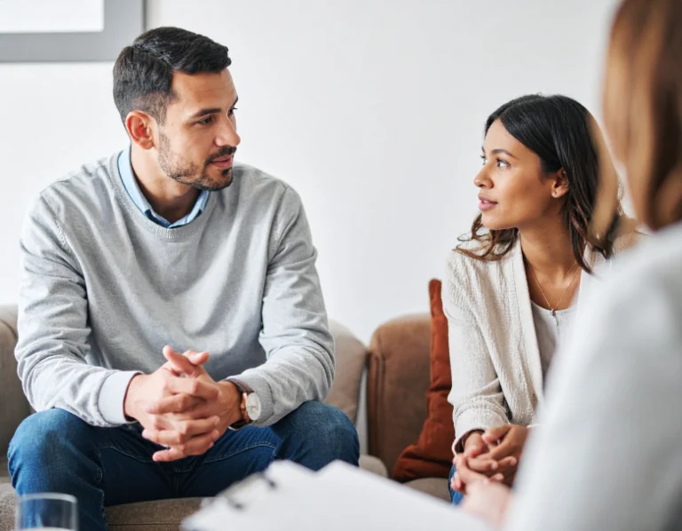 From Renew Hope and Healing: A man and a woman sit on a couch, talking and facing each other during marriage counseling, while another person sits across from them, partially visible.