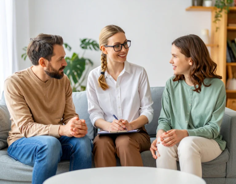 From Renew Hope and Healing: A man and woman sit on a couch talking with a professional woman holding a clipboard, suggesting a marriage and family therapy session in a bright room.