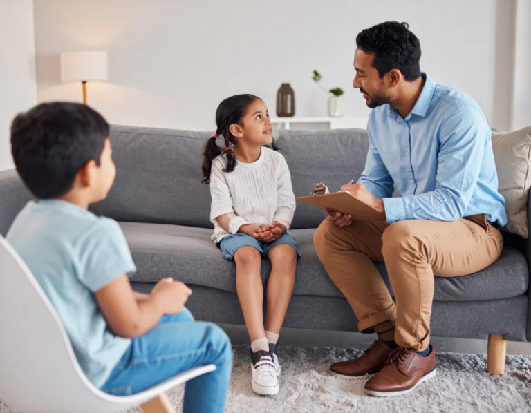 From Renew Hope and Healing: A man with a clipboard talks to a young girl on a couch while another child sits nearby in a chair, illustrating a Family Counseling session.