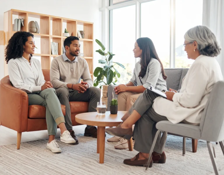 From Renew Hope and Healing: A couple sits on a couch talking with two women, one holding a clipboard, in a modern, well-lit office setting during couples counseling.