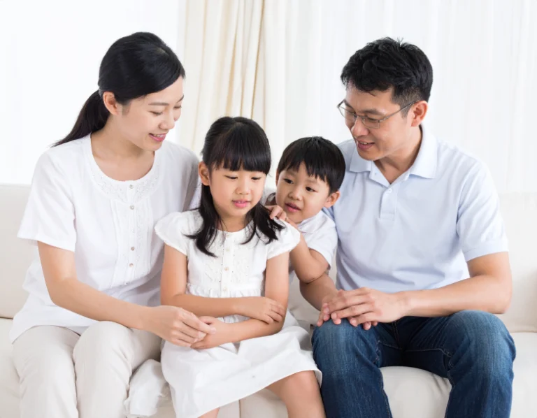 From Renew Hope and Healing: A family of four sits together on a white sofa, with two adults and two children, all wearing light-colored clothing, smiling and interacting—radiating the harmony that family counseling can help nurture.